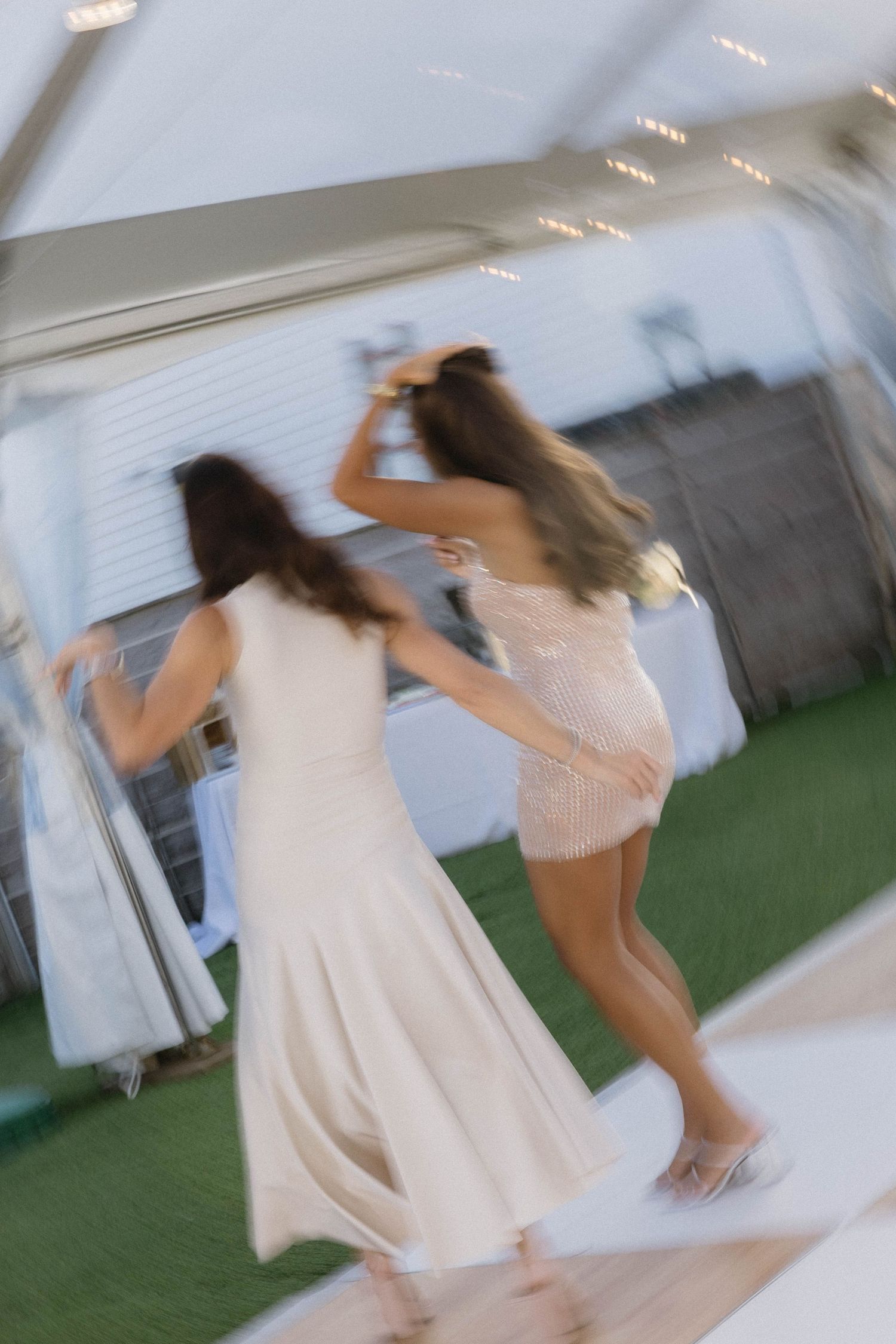 Blurred motion shot of two women dancing energetically on a checkered dance floor at a wedding.