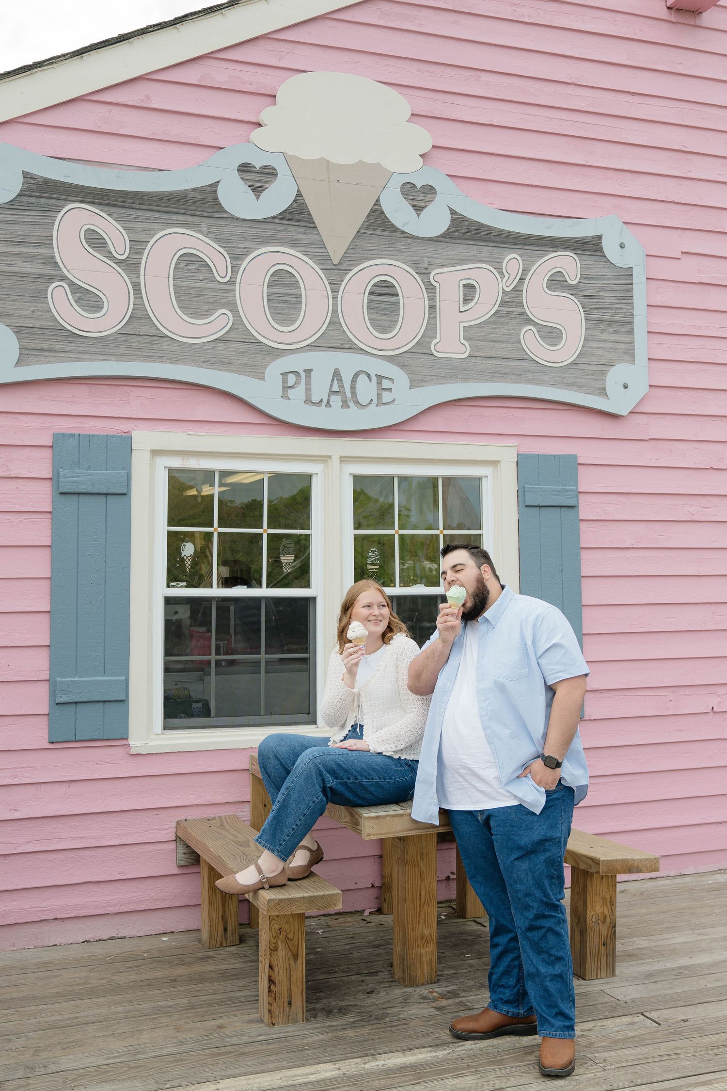 Couple enjoying ice cream cones outside Scoop's Place, a charming pink ice cream shop with blue shutters.