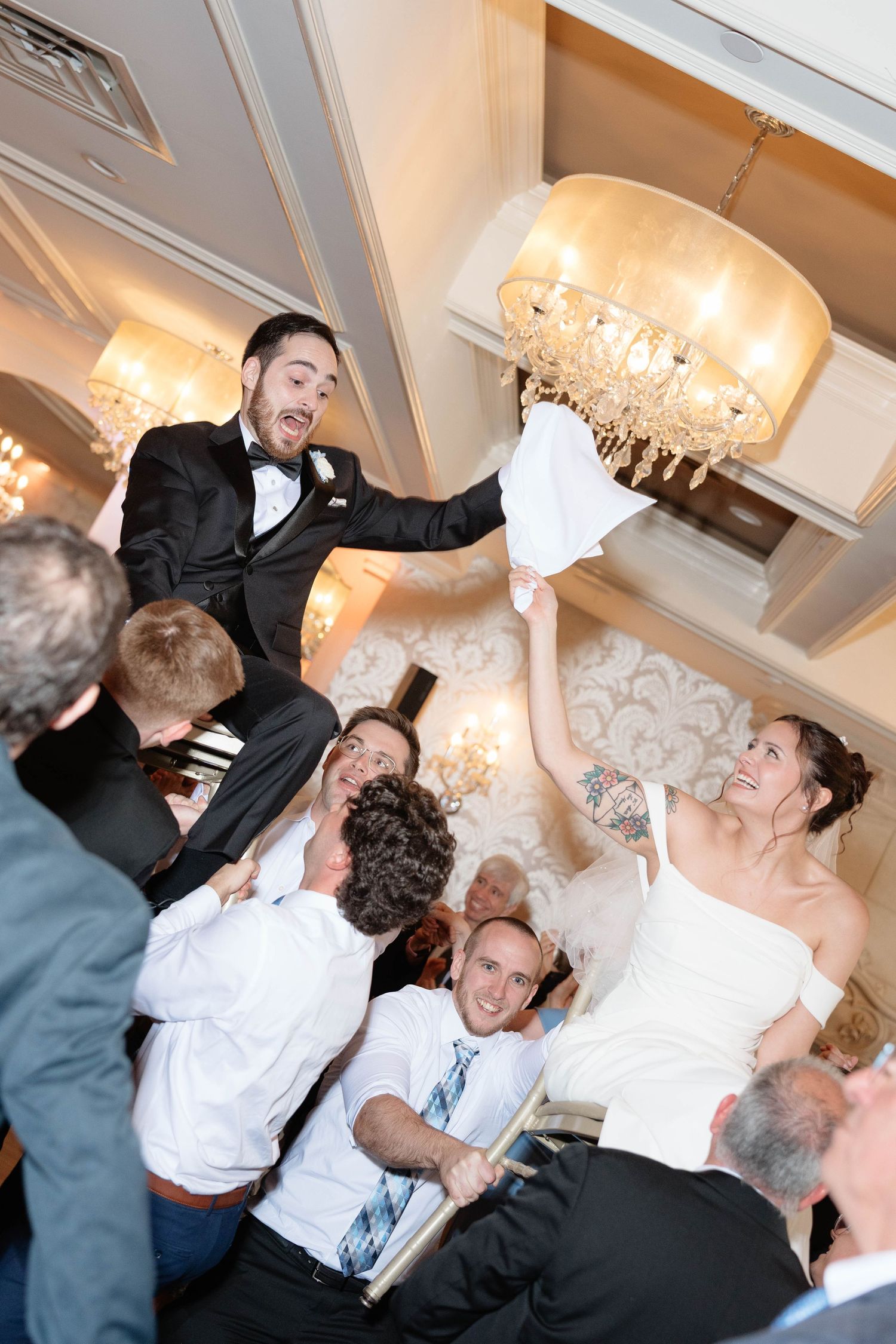 Bride and groom are lifted on chairs during lively Jewish wedding hora dance celebration.