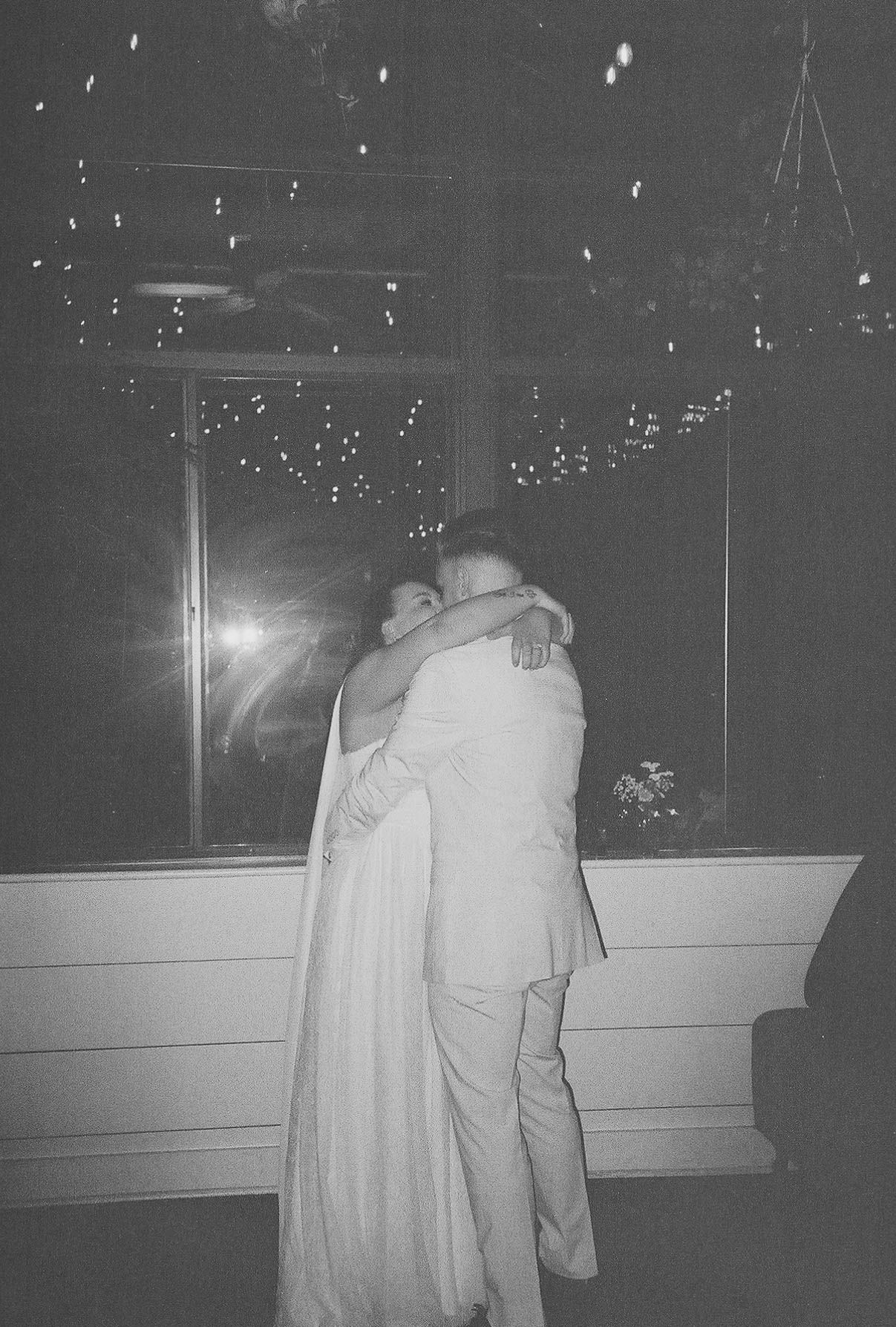 Black and white photo of a couple sharing a romantic embrace on a dance floor at a wedding reception.
