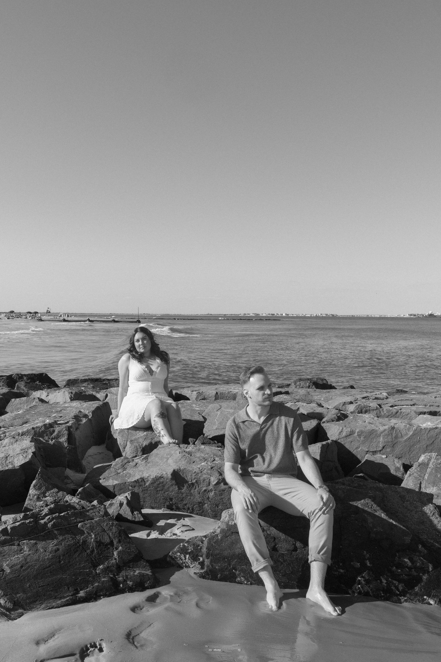Black and white photo of couple sitting on coastal rocks with ocean view behind them.