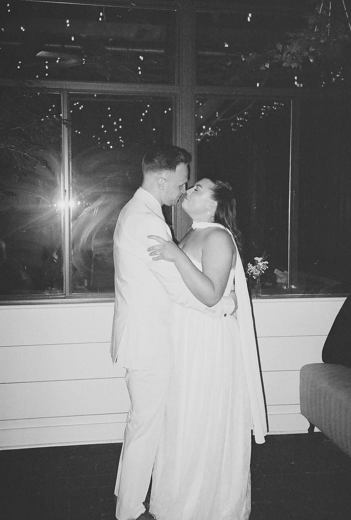 Black and white photo of a couple sharing a romantic kiss during their first dance at a wedding reception.