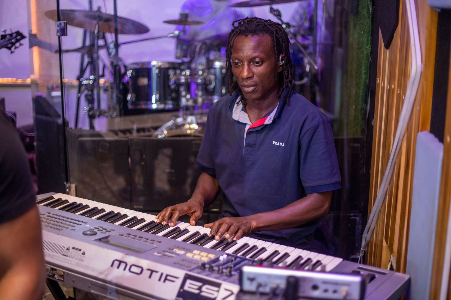 Man playing a Yamaha Motif ES7 keyboard synthesizer in a music studio with drums in the background.