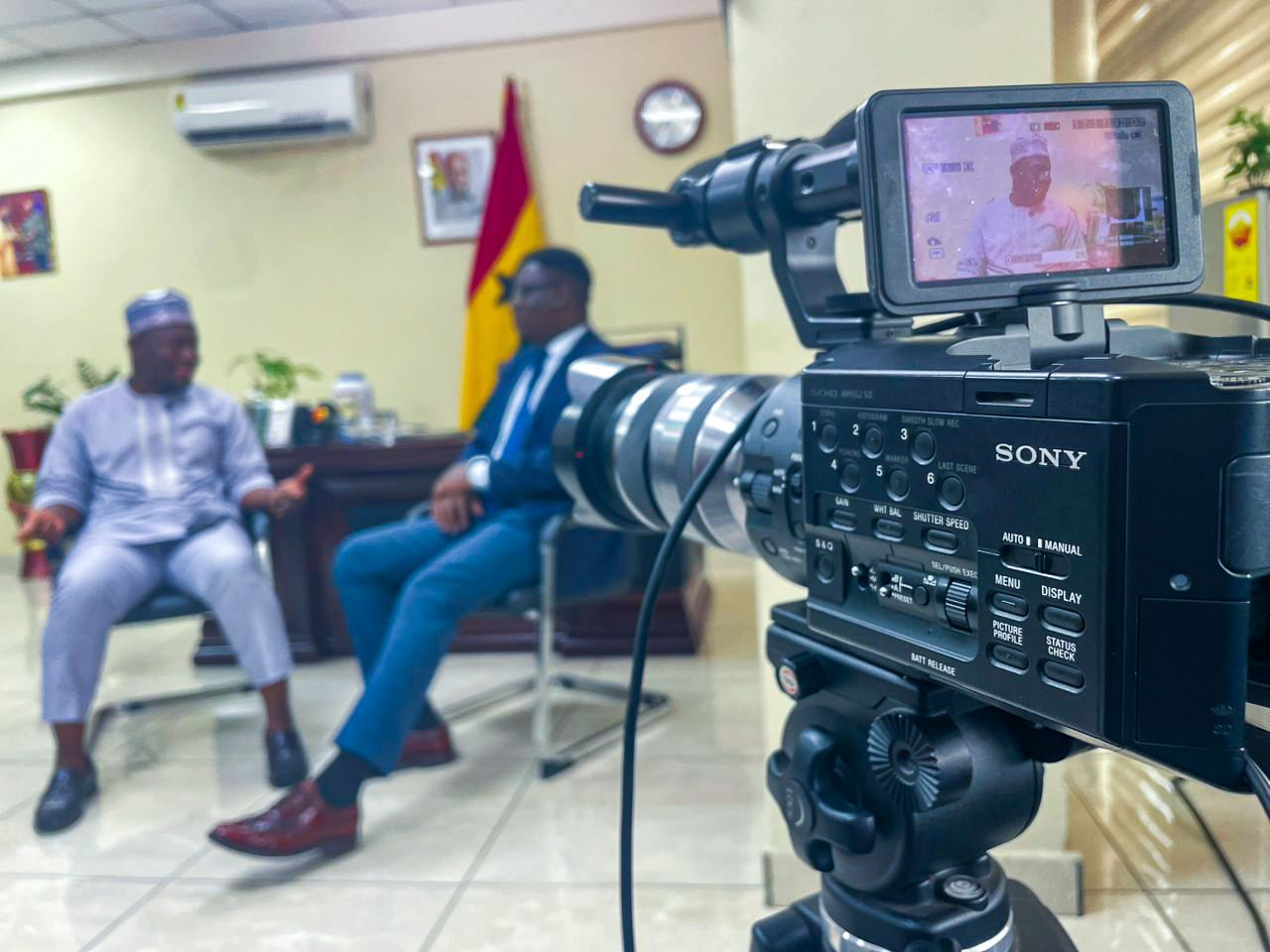 Sony professional video camera filming an interview with two men in a colorful office setting.