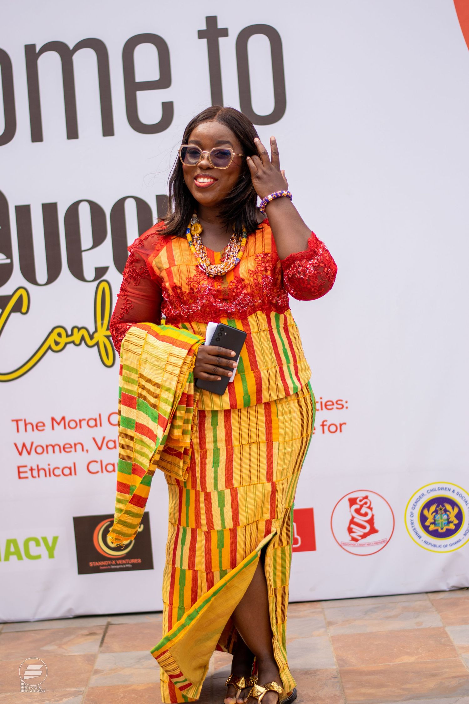 Woman in vibrant Kente cloth outfit posing at Queens Conference event in Ghana.