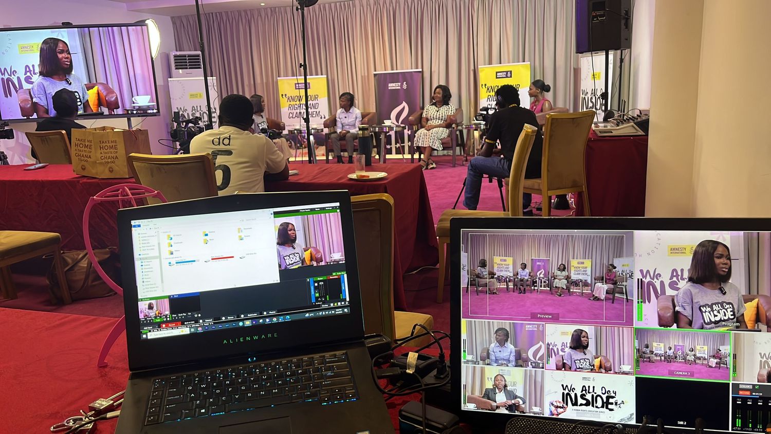 A hybrid event setup with a panel discussion on stage and a laptop showing a video conference call in the foreground.