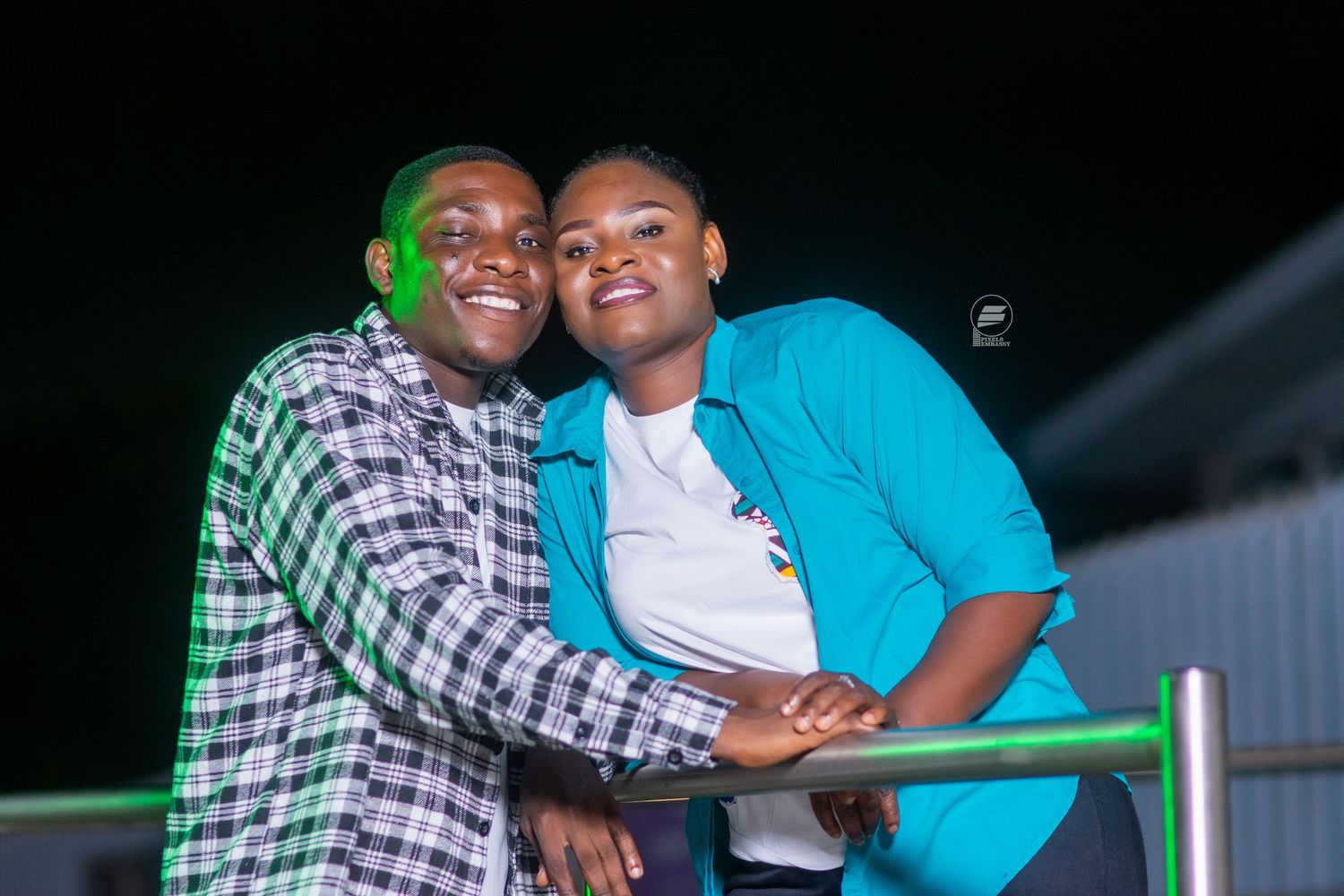 Two smiling friends pose together outdoors at night, one in a plaid shirt and one in a blue jacket.