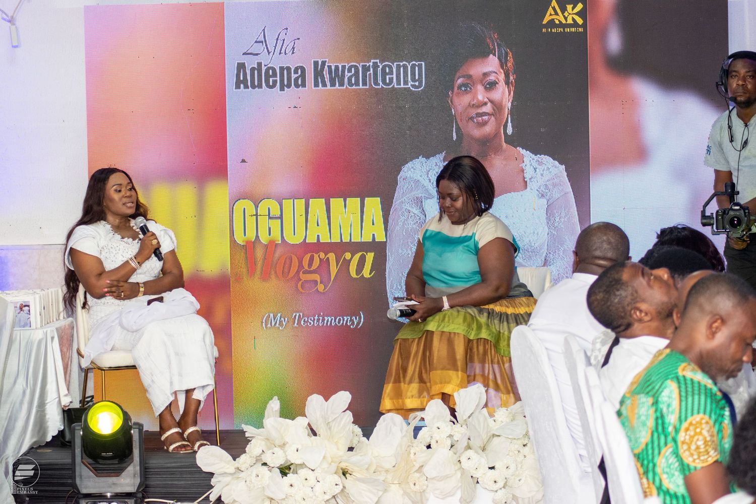 Woman in white outfit speaking on stage at Adepa Kwarteng Noguama Mogya album launch event.
