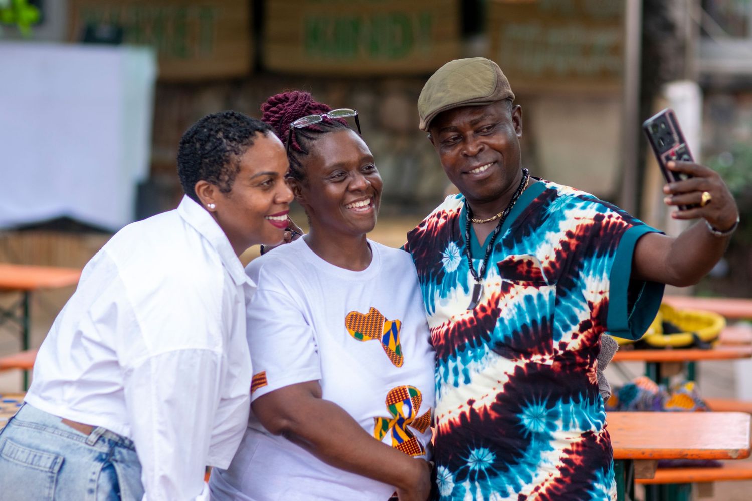 Three smiling African friends taking a selfie together at an outdoor cultural festival event.