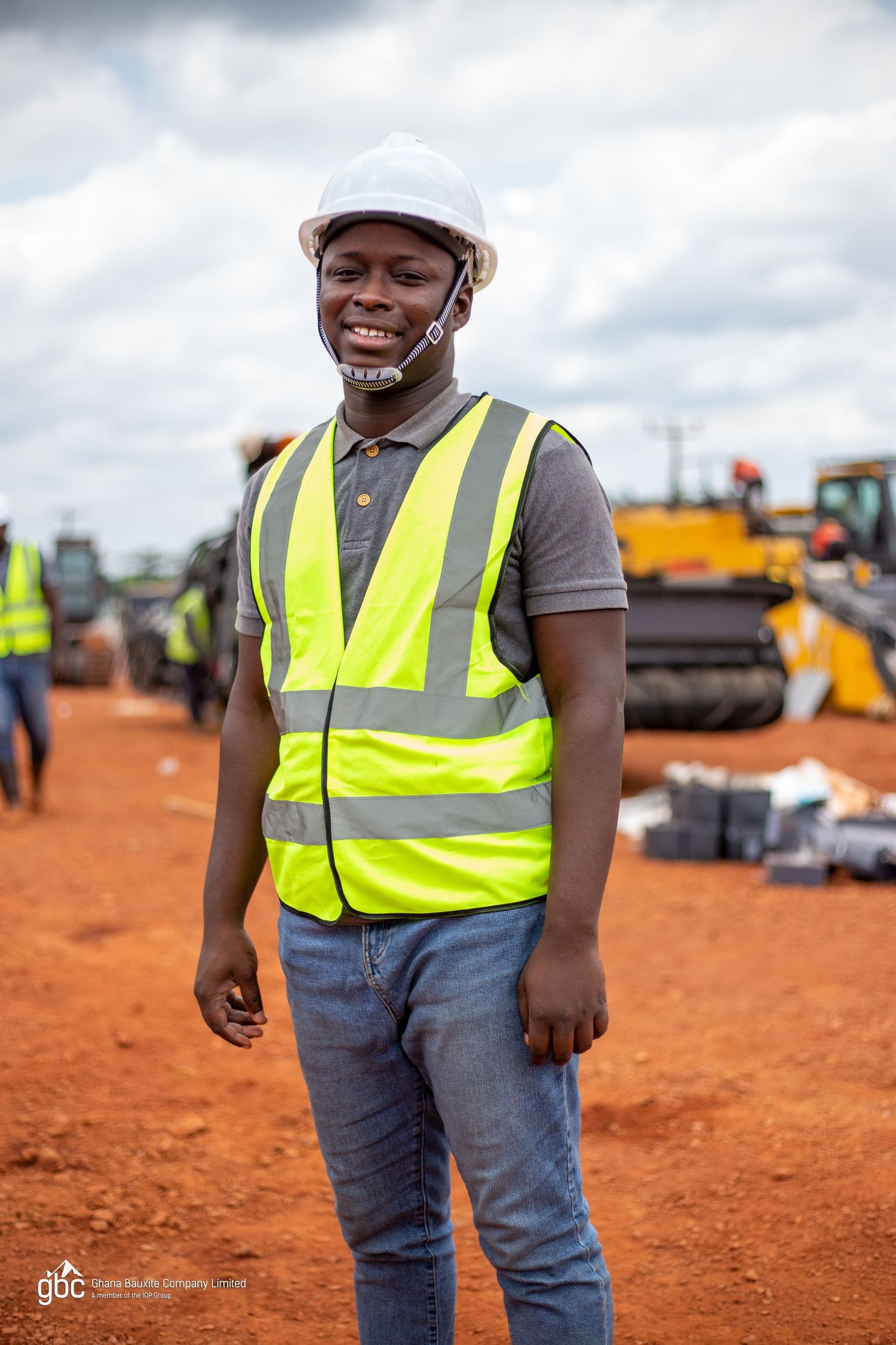 Construction worker smiling in yellow safety vest and white hard hat at a job site.