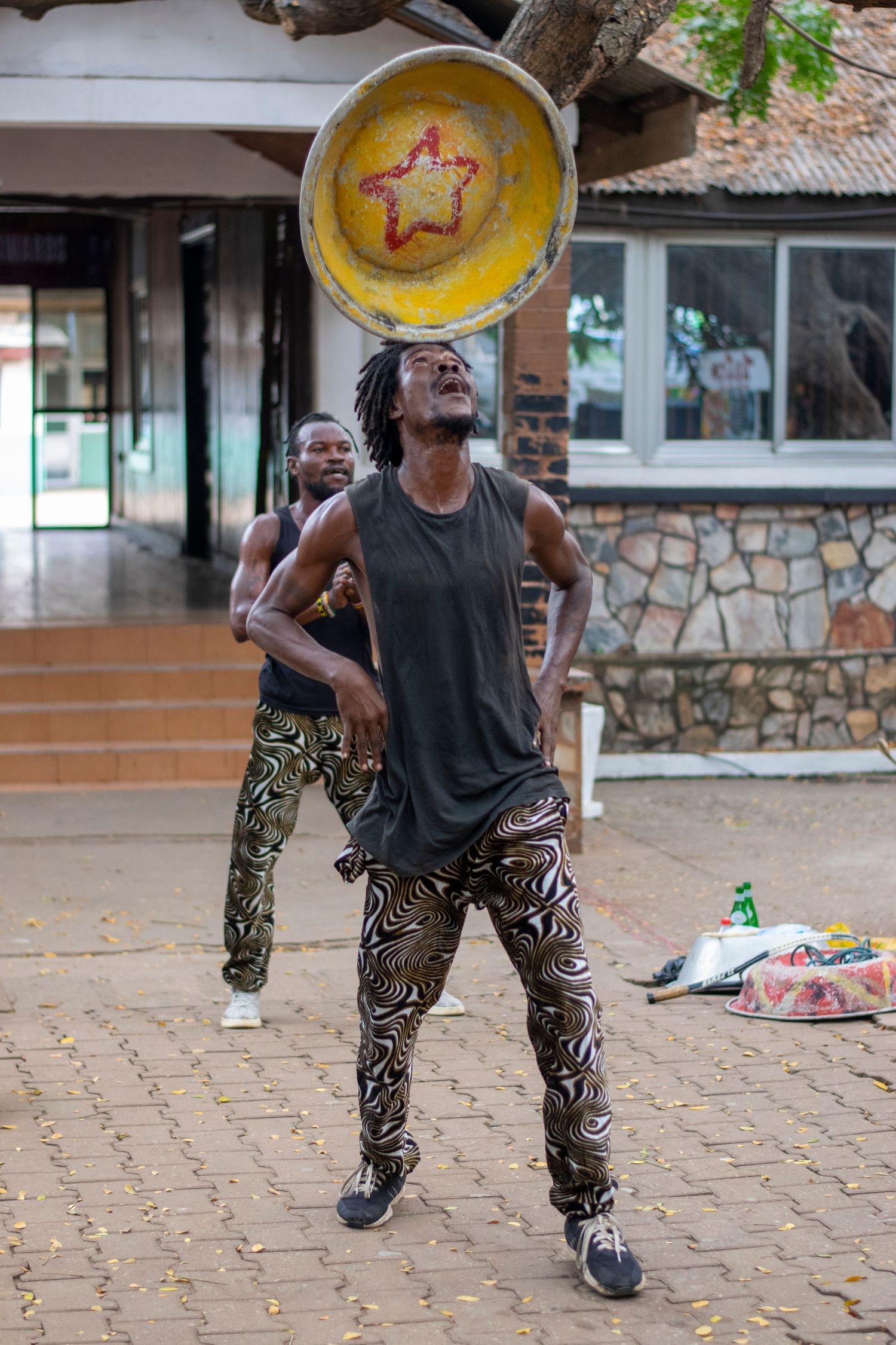 African street performer balancing a large decorative bowl on his chin at an outdoor market.
