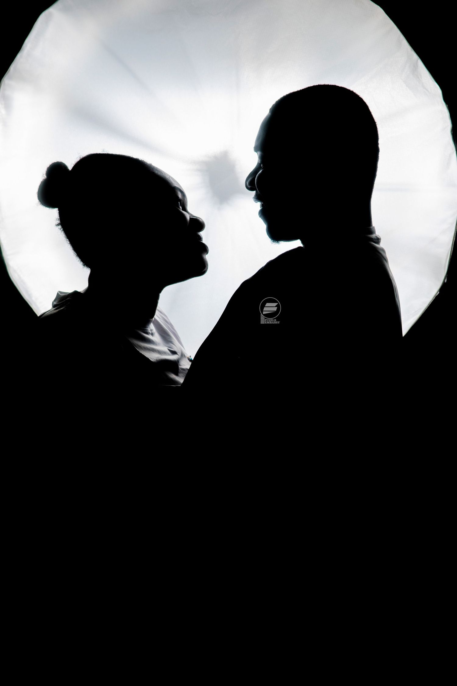 Silhouette of a couple facing each other against a bright circular light backdrop in black and white.