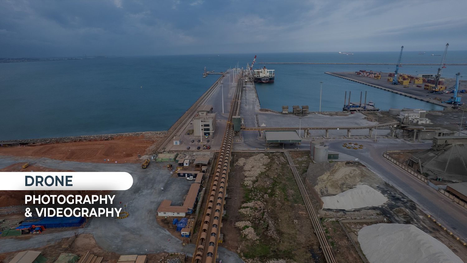 Drone aerial photography of a coastal port with railway tracks, cargo ships, and ocean views.