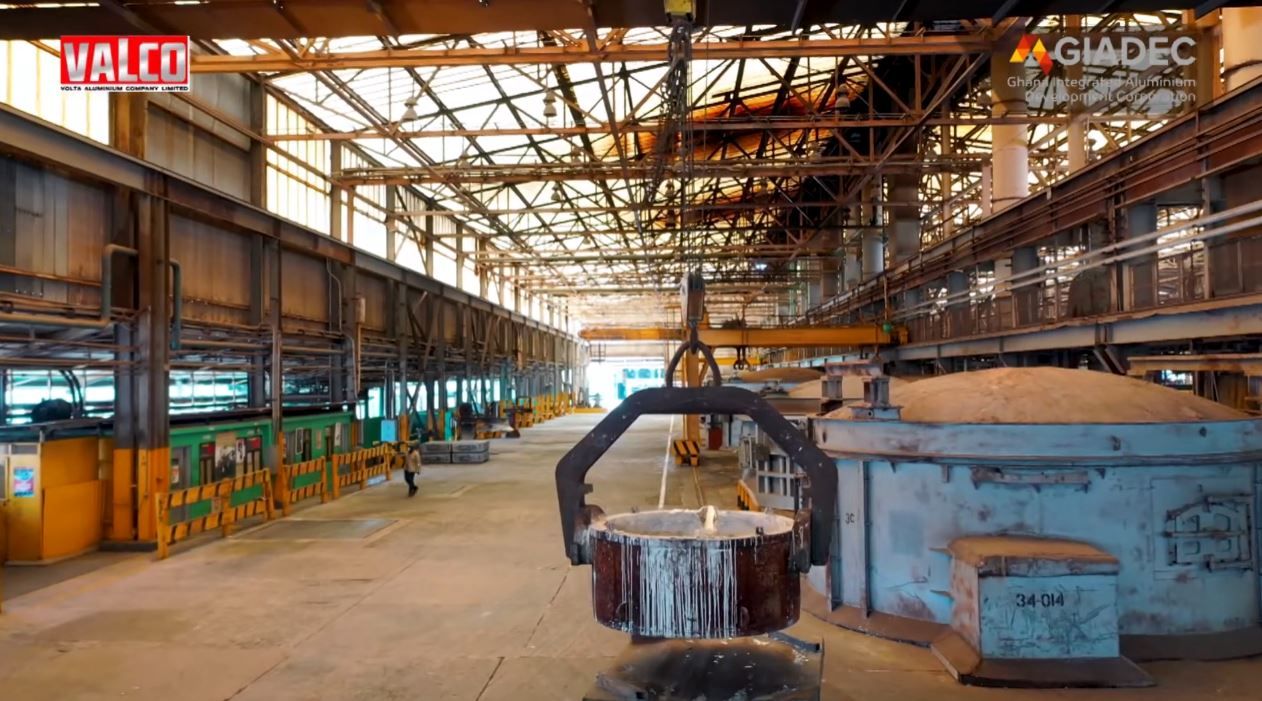 Industrial factory interior with overhead crane lifting molten metal at VALCO aluminum smelting facility.