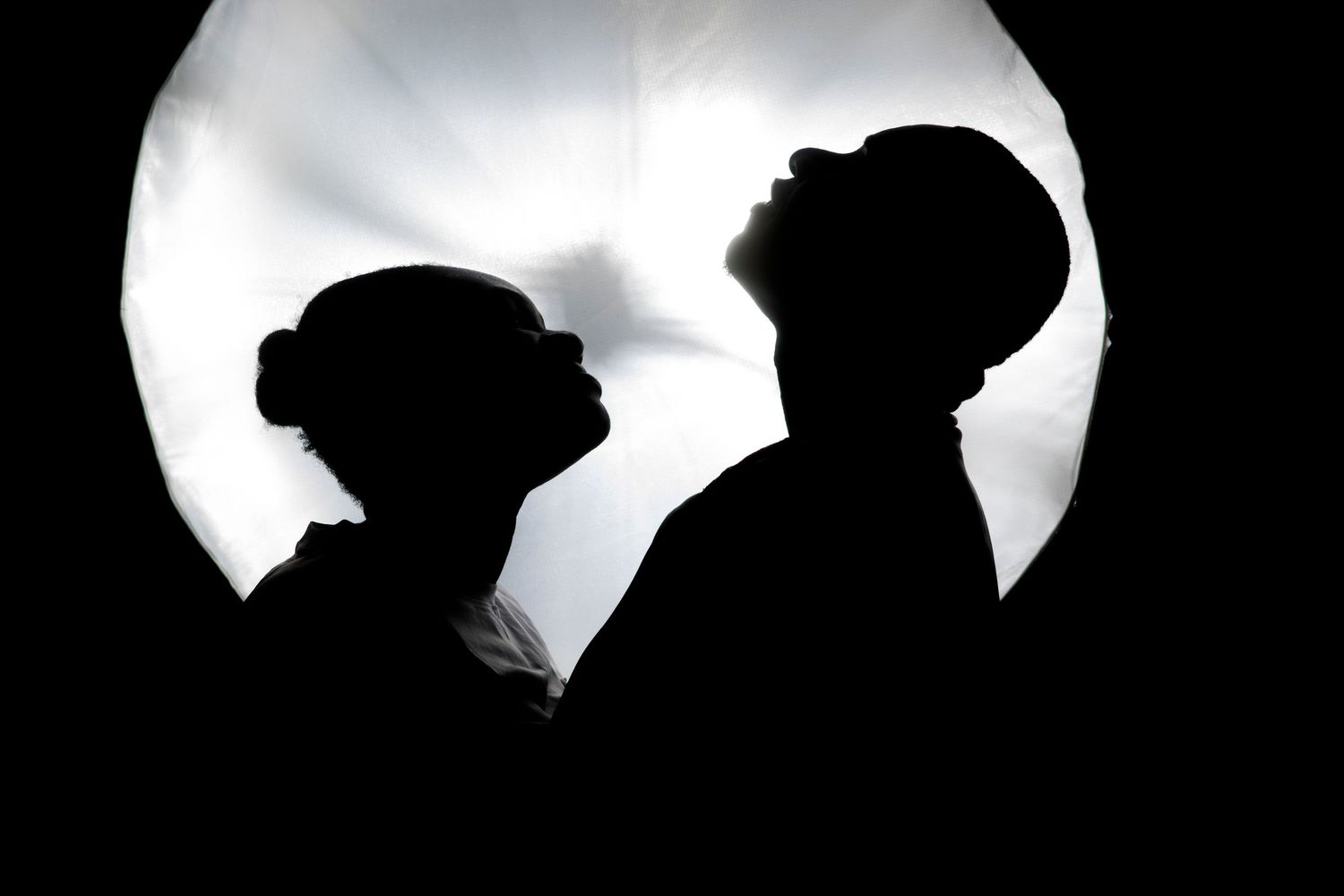 Silhouette of two people against a bright circular light, creating a dramatic contrast in black and white.