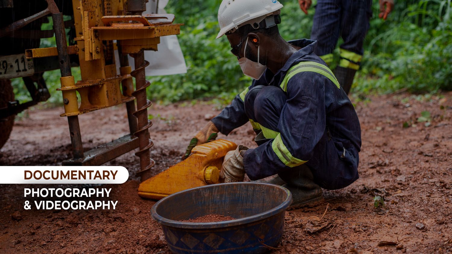Documentary photographer capturing a worker in safety gear operating mining equipment in a muddy outdoor environment.