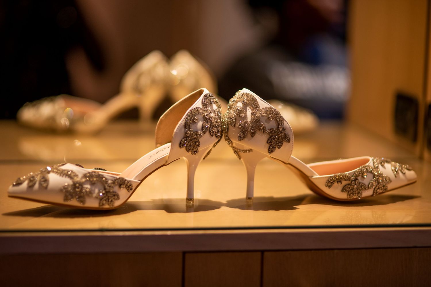 Elegant white and gold embroidered high heel shoes displayed on a reflective surface.