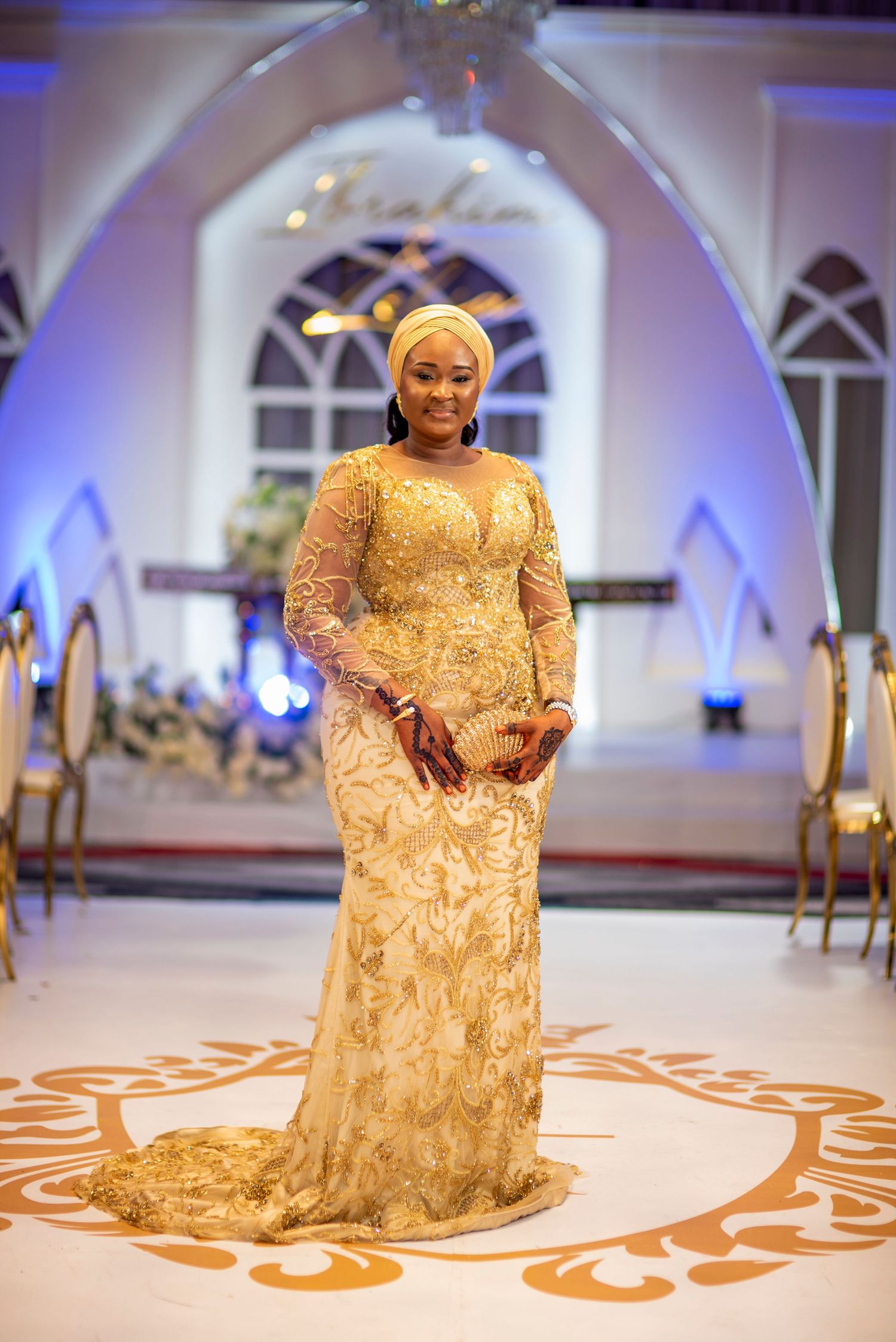 Bride in stunning gold embroidered lace gown posing in elegantly decorated wedding hall.