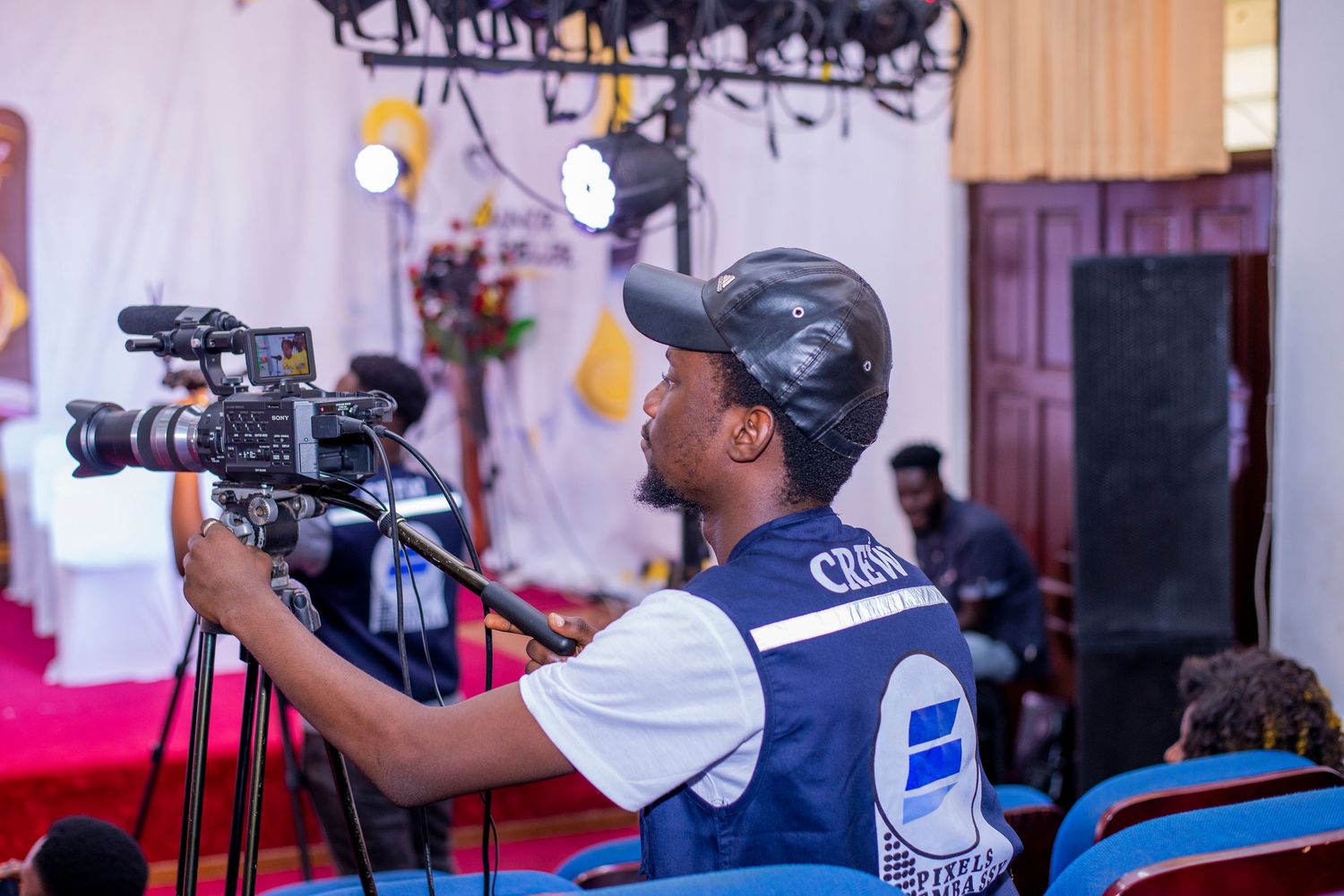 Cameraman filming an event with a professional video camera while wearing a blue vest.
