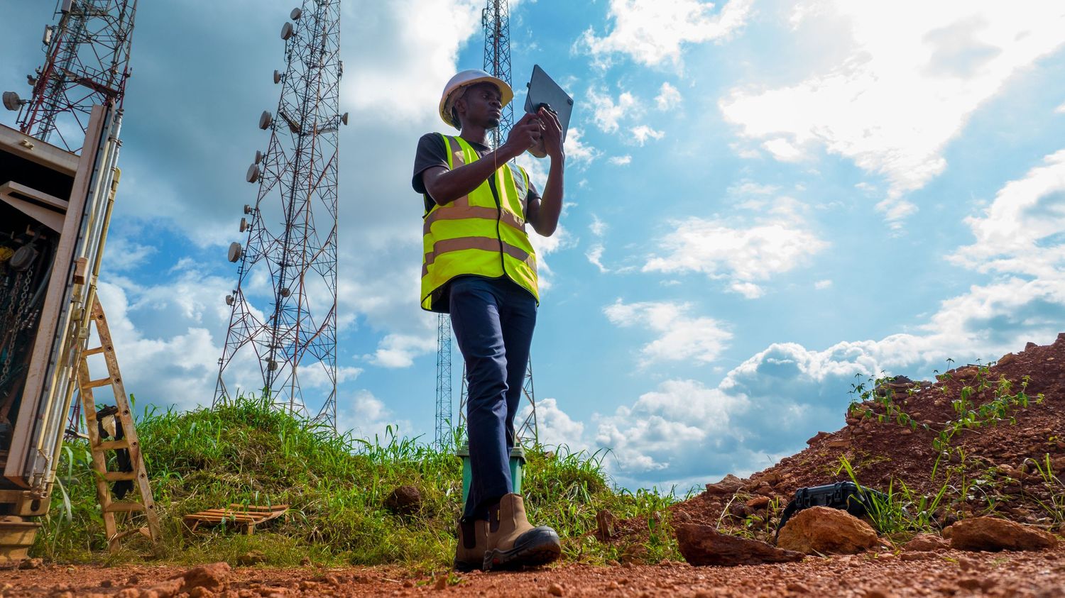 Female engineer in safety vest using tablet near telecommunications towers outdoors.