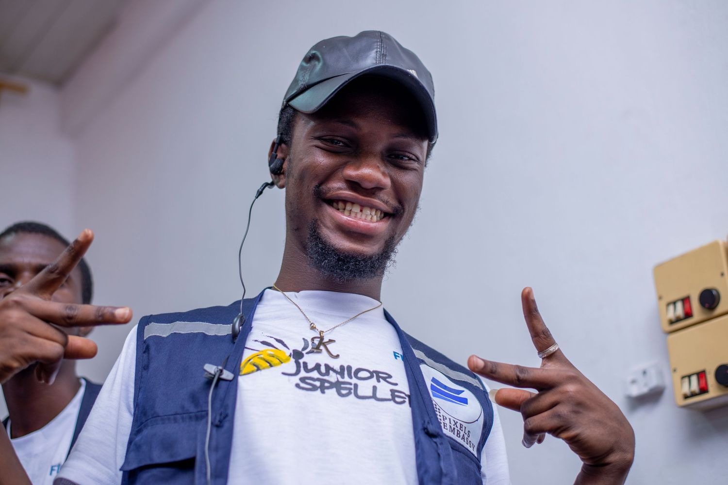 Cheerful young man in a Junior Speller vest smiles and poses with hand gestures at an event.