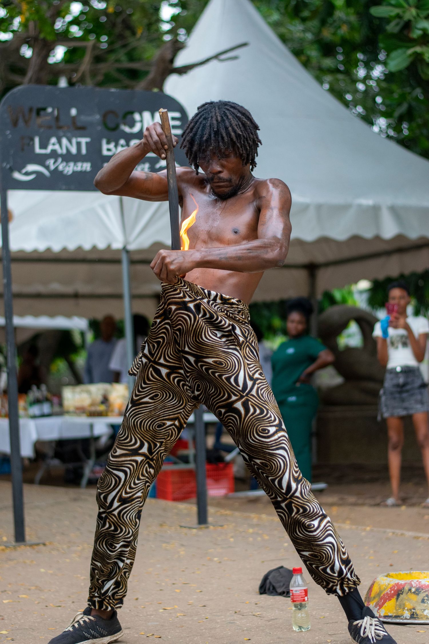 Shirtless African fire performer holding a flaming torch at a plant-based vegan market event.