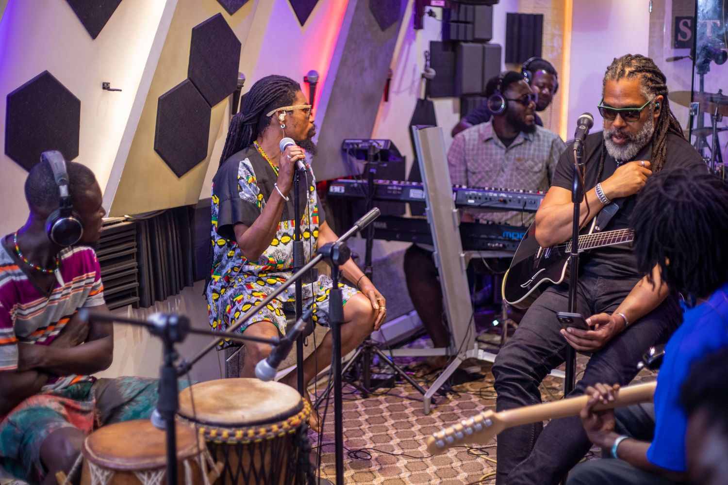 Live African music band performing with djembe drums, guitar, and vocals in a modern studio setting.