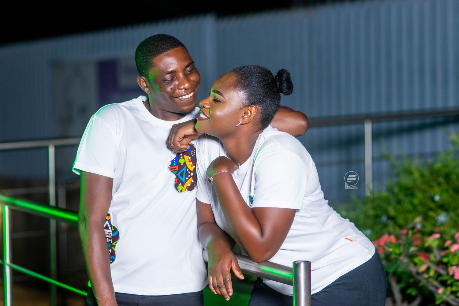 Two young people in white t-shirts share a joyful moment outdoors at night, smiling at each other warmly.