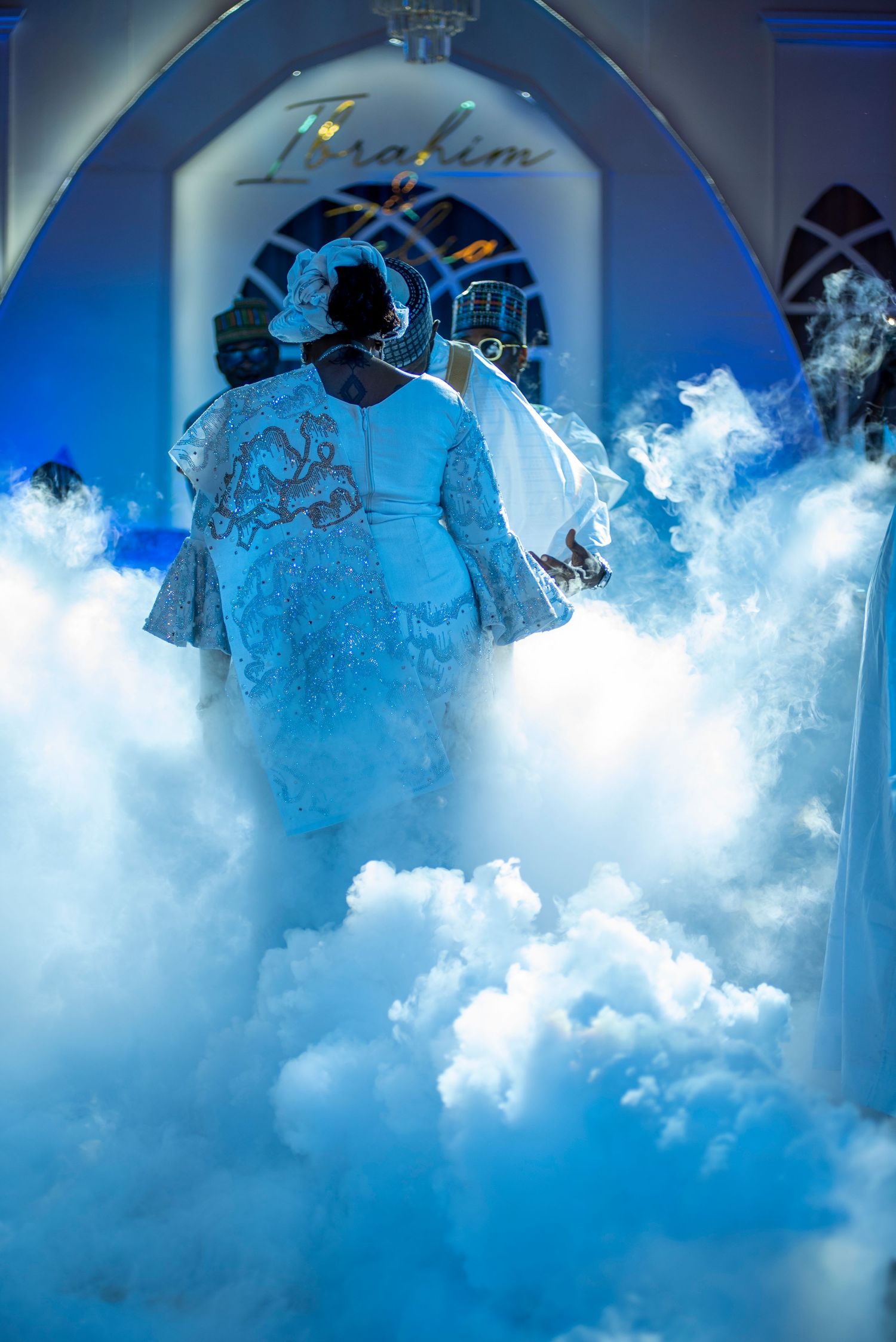 Couple entering wedding venue through dramatic dry ice fog under blue lighting.