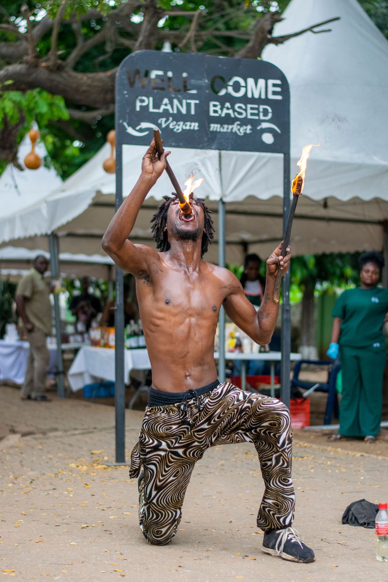Shirtless African fire eater kneeling while performing at a Welcome Plant Based Vegan Market.