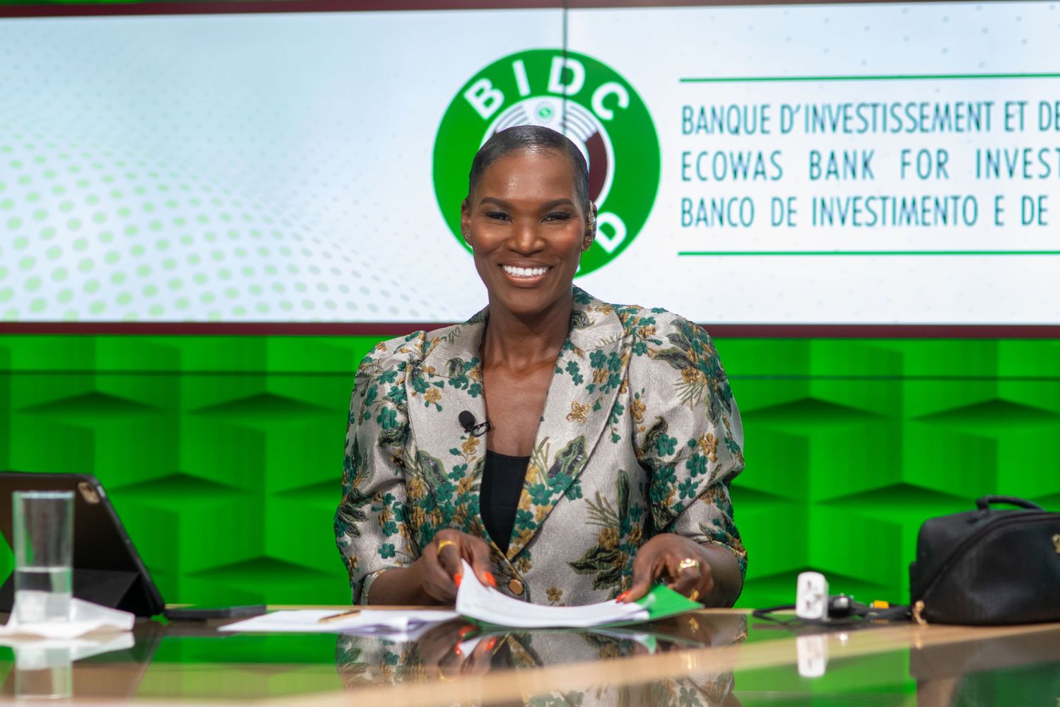 Woman smiling at desk in front of ECOWAS BIDC bank green branded backdrop.