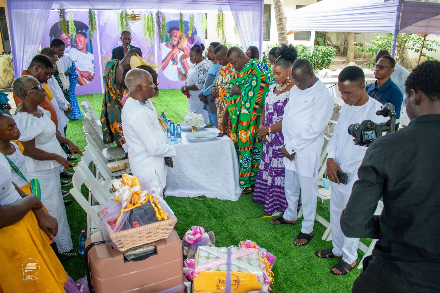 Traditional African wedding ceremony with guests in colorful kente cloth exchanging gifts outdoors.