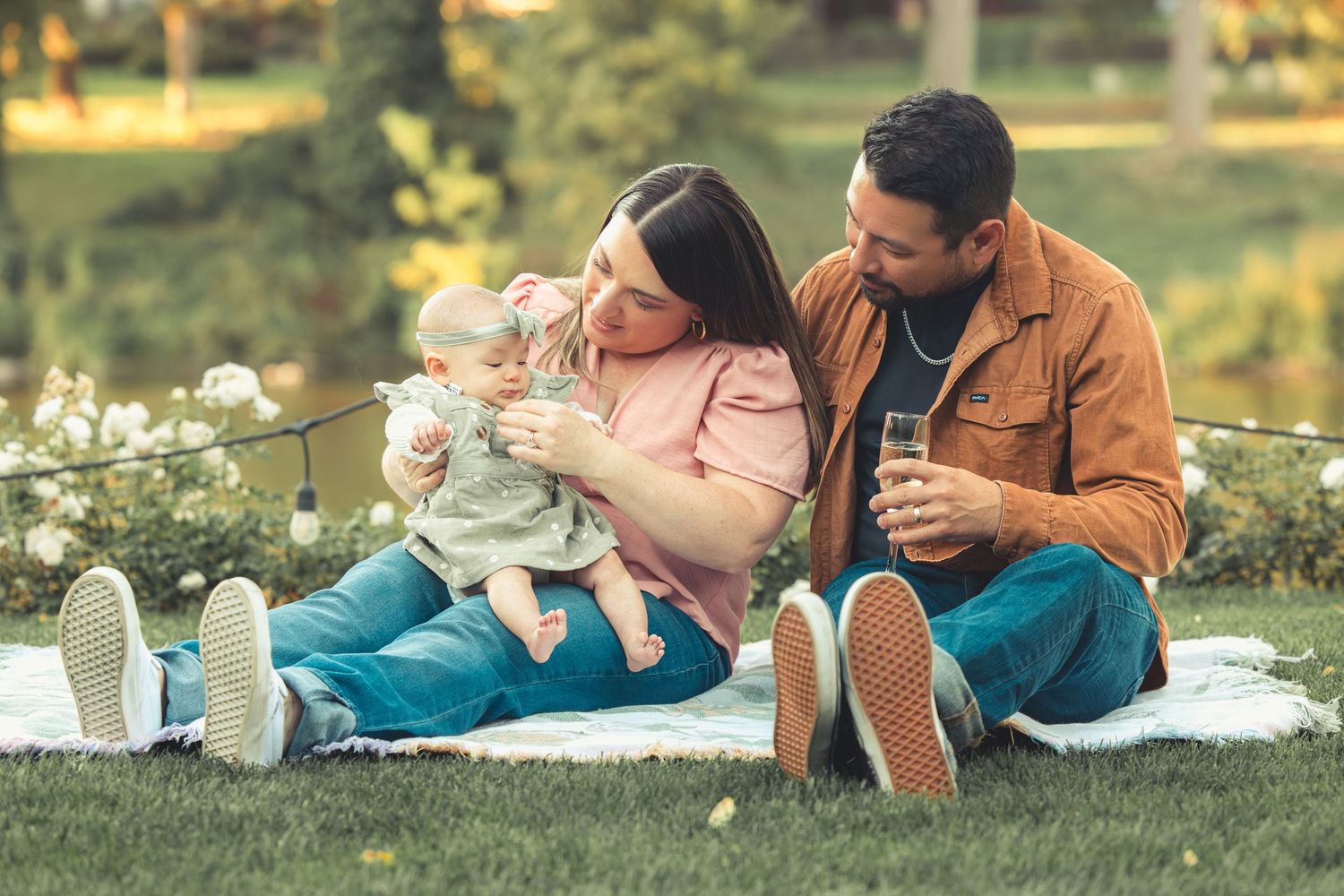 Family with baby enjoying a picnic on a blanket in a lush green park.