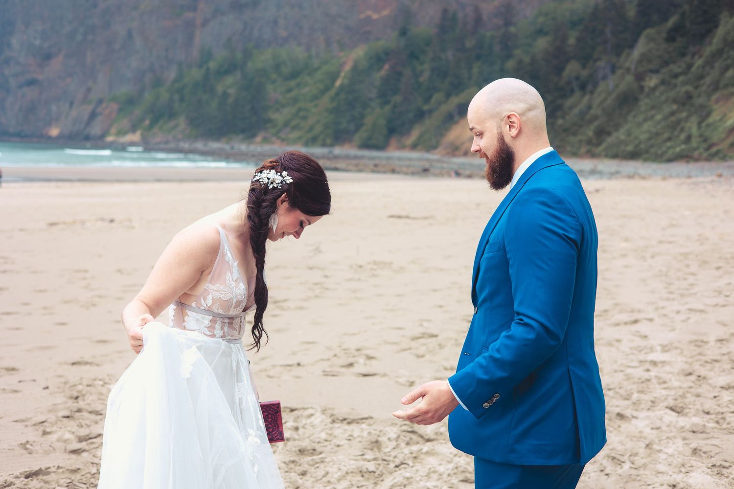 Bride and groom exchange vows on a sandy beach with lush green cliffs in background.