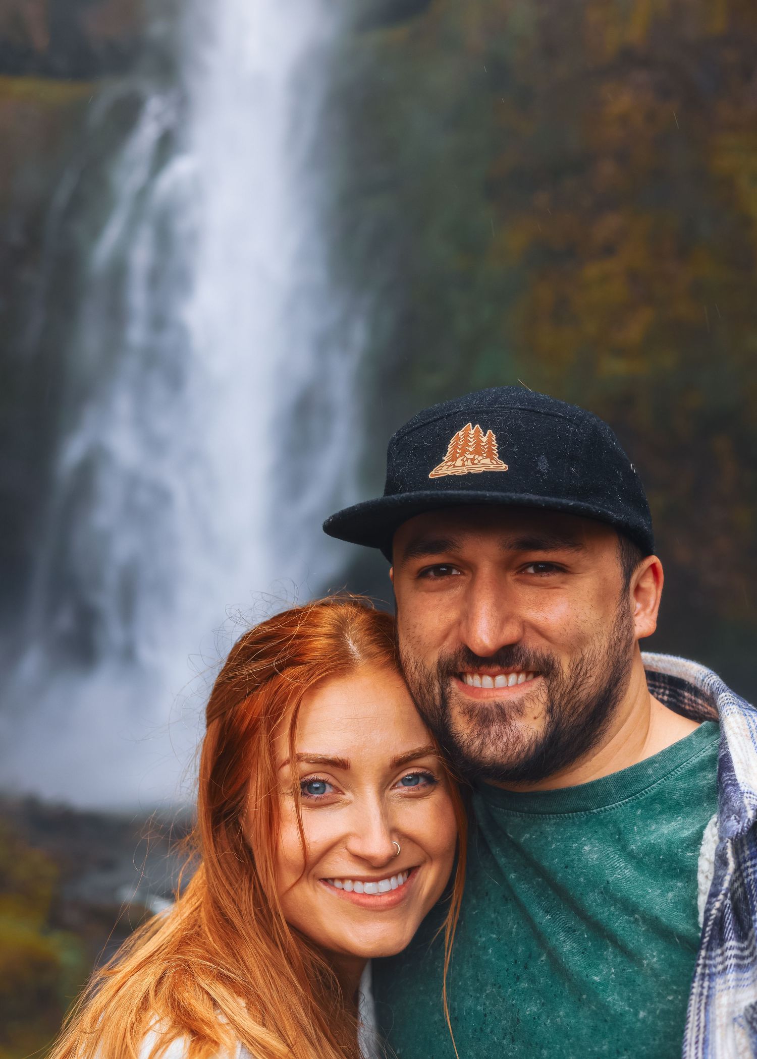 A smiling couple poses together in front of a stunning waterfall in Oregon.