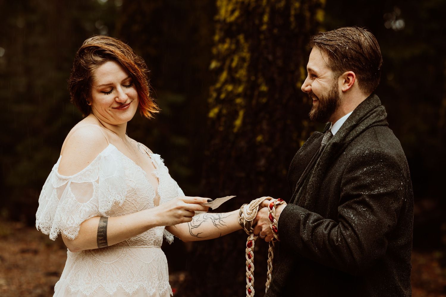 Smiling bride and groom exchange vows during an outdoor handfasting wedding ceremony in the woods.
