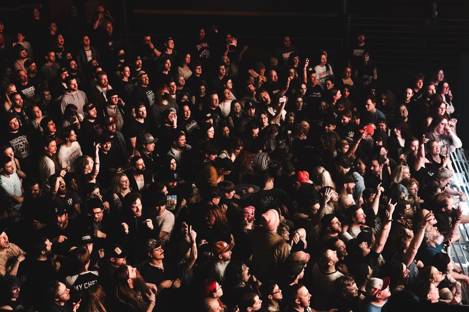 Dense crowd of concert-goers packed together at a live music event in a dark venue.