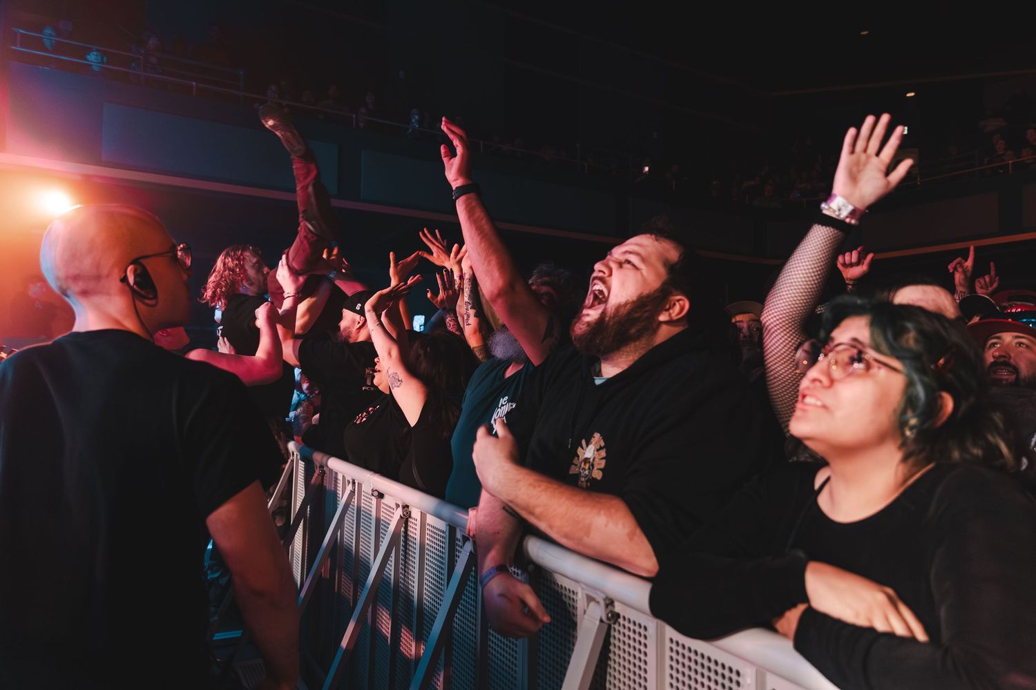 Excited concert fans cheer and raise hands at barrier during energetic live music performance.