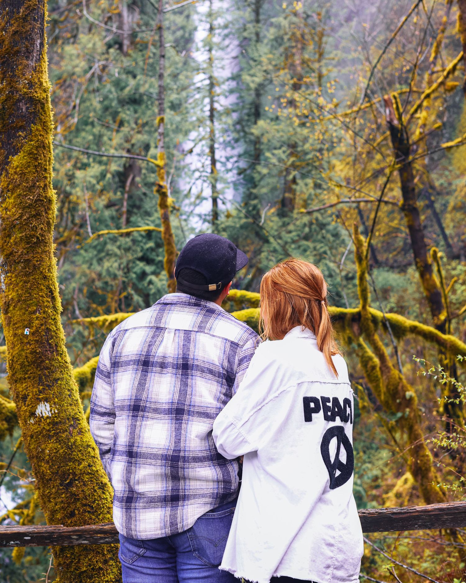 A couple embraces while gazing into a lush moss-covered Pacific Northwest forest.