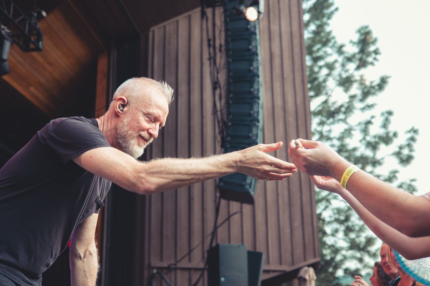 Male performer leaning off stage reaching out to touch fans hands at outdoor concert.