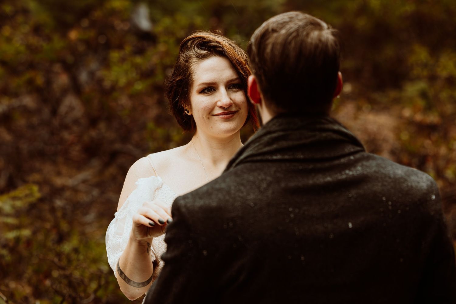 Bride smiles softly at groom during intimate outdoor forest elopement ceremony on a rainy day.