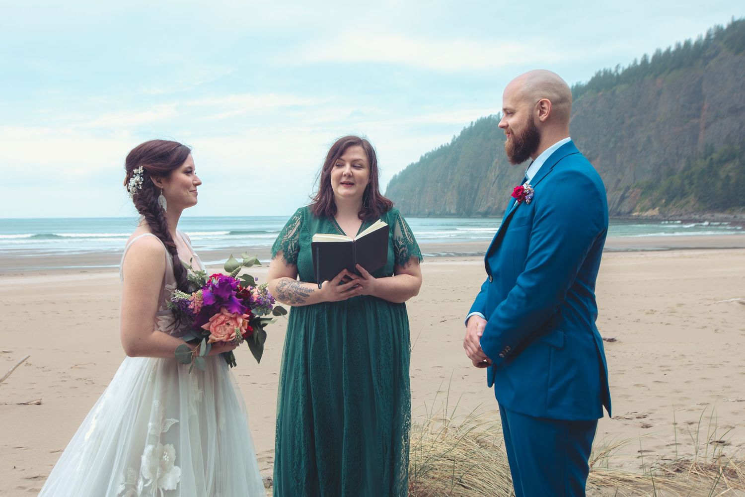 Couple exchanges vows with officiant in green dress during intimate beach wedding ceremony.