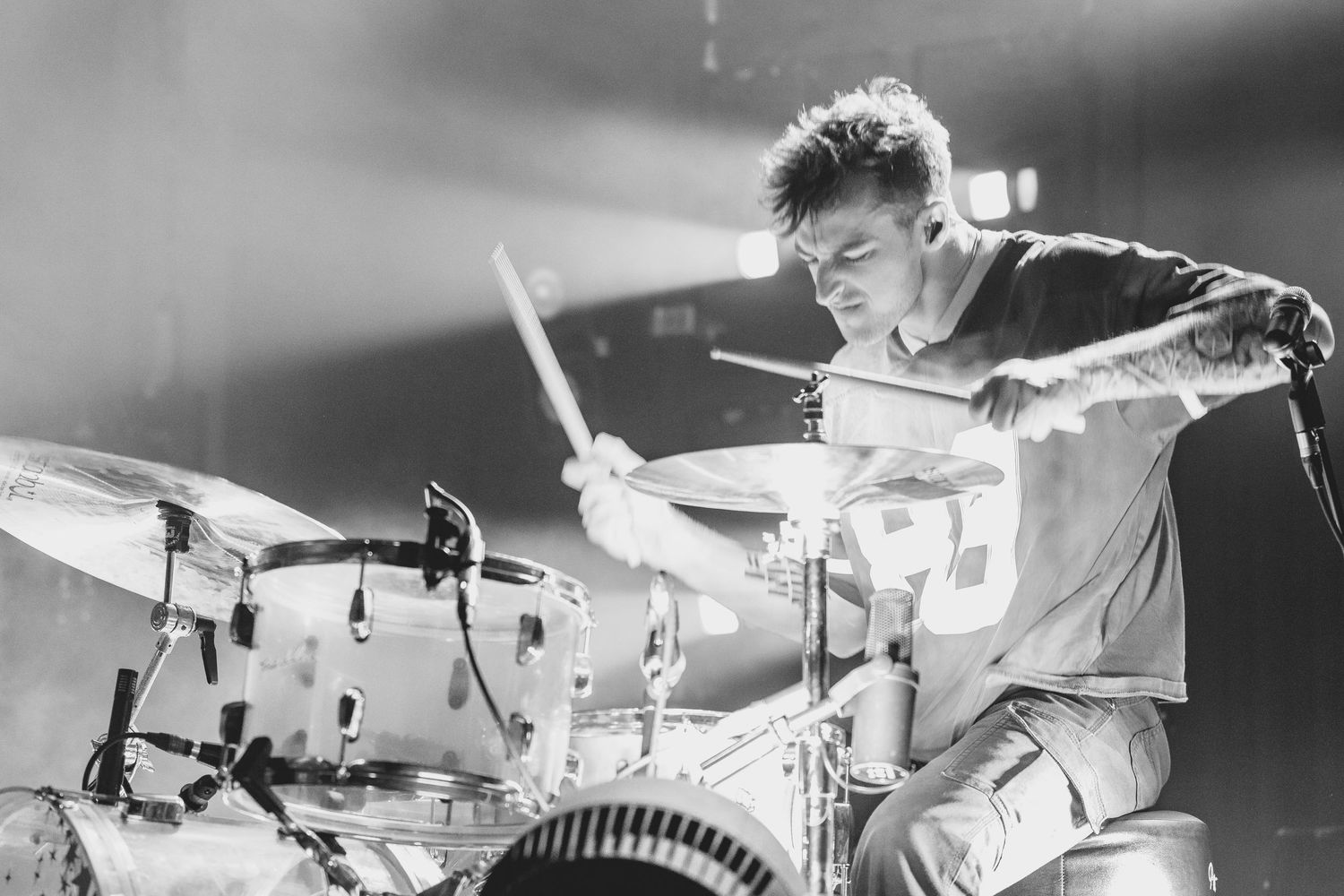 Tattooed male drummer playing intensely on stage in a black and white concert photo.