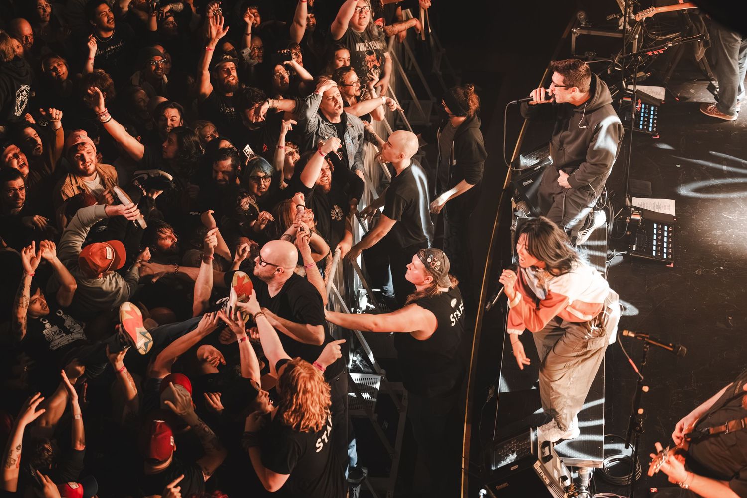 Aerial view of a vocalist leaning into the crowd during an intense live rock concert.