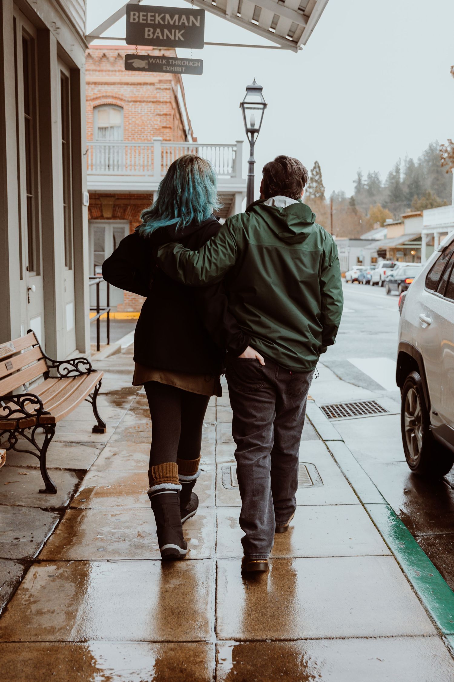 Couple walking arm in arm on a rainy sidewalk near Beekman Bank in a small town.
