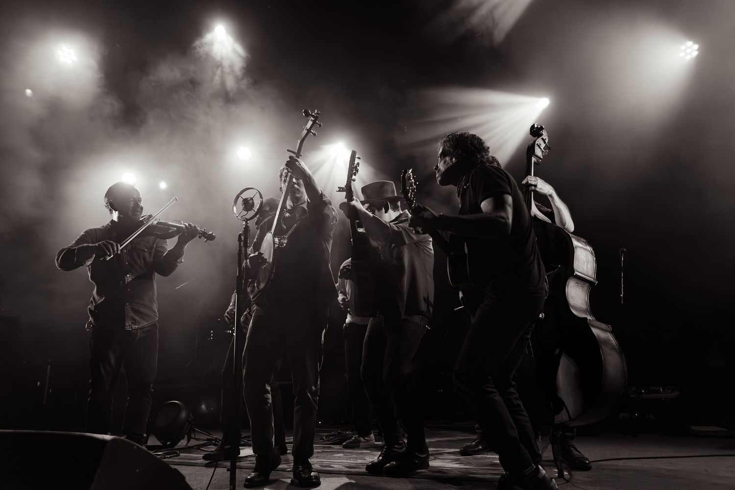Black and white shot of folk band with violin, banjo, and double bass on stage.