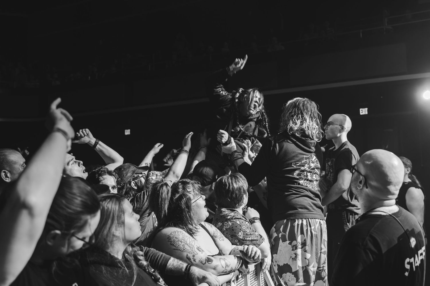 Black and white photo of crowd surfing at a packed rock concert with excited fans reaching upward.