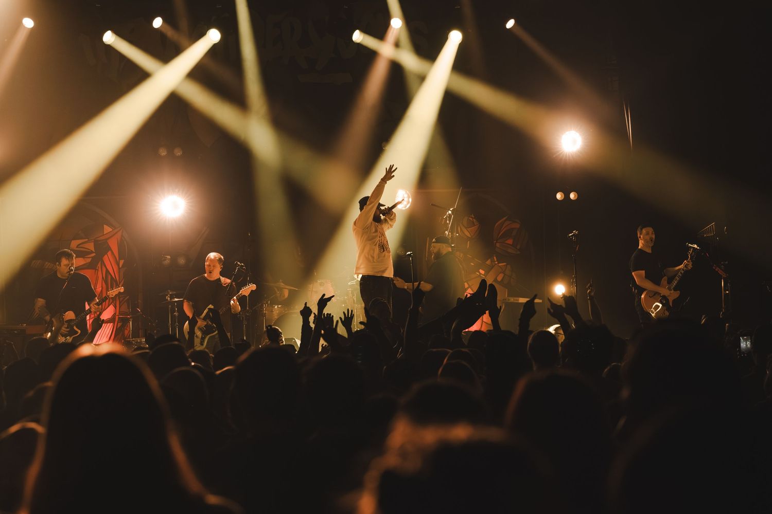 Band performing on stage with golden spotlights and crowd silhouettes in the foreground.