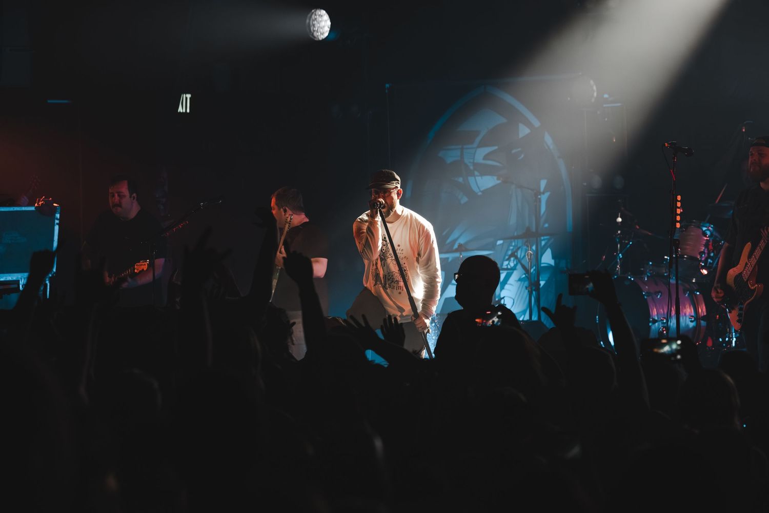 Band performing on a dimly lit stage with blue spotlights and a crowd in the foreground.