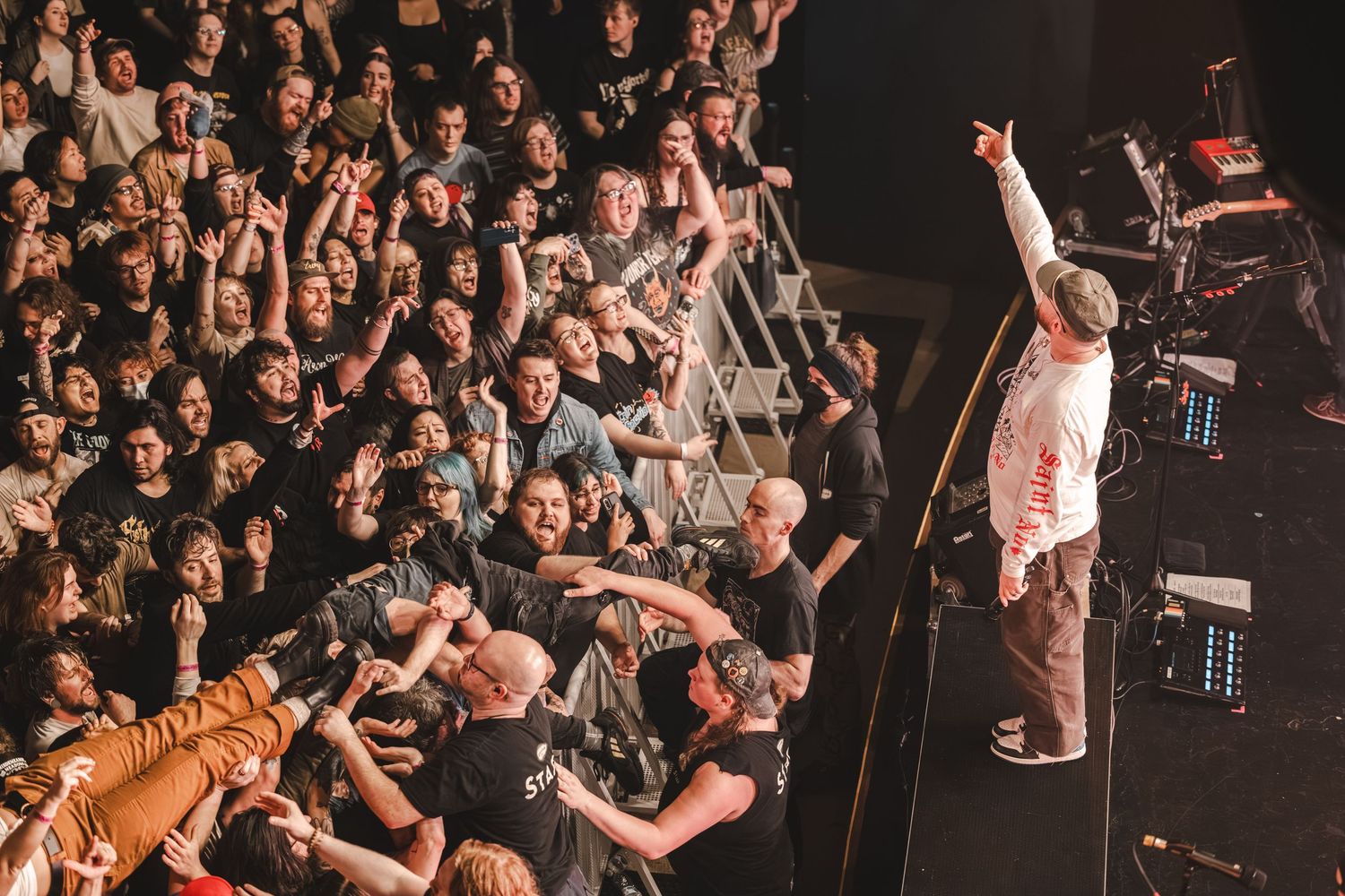 Performer raises arm to energetic crowd in a packed concert venue during live show.
